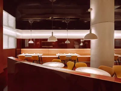 A modern restaurant interior with red walls, white pendant lights, and yellow chairs.