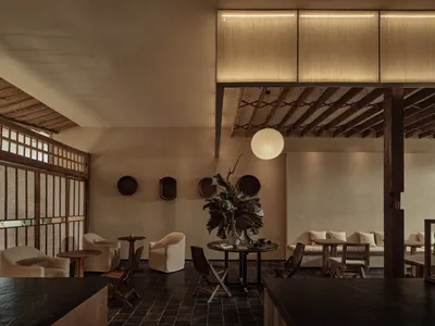 A modern restaurant interior featuring wooden furniture, plaster walls, and fabric seating.