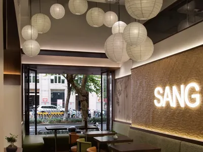 A modern cafe interior with hanging paper lanterns, wooden furniture, and upholstered seating.