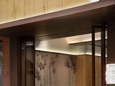 A modern restaurant entryway featuring glass and wood materials with recessed lighting.