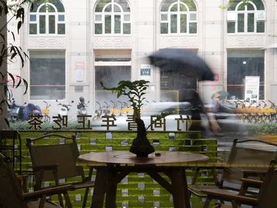 A cozy coffee shop with glass doors, wooden tables, and chairs, viewed from inside.