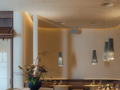 A modern restaurant interior with white walls, wooden furniture, and hanging pendant lights.