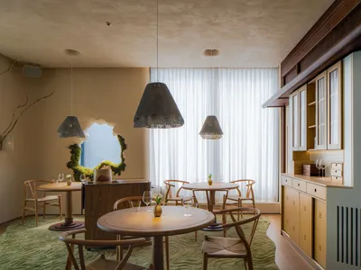 Modern restaurant interior with wooden tables, fabric curtains, and a window showcasing the outdoors.