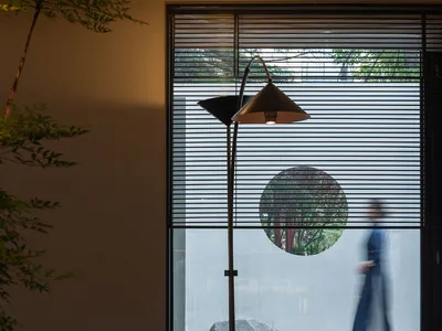 A modern restaurant interior featuring wooden tables, metallic floor lamp, and plants.