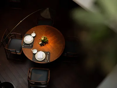 A round wooden table set for dining in a modern restaurant setting, featuring plush black chairs and minimalist decor.