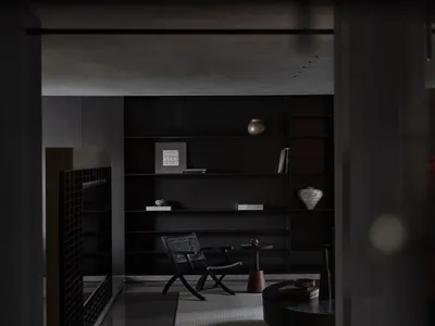 Modern minimalist living room featuring dark wood and metal accents, with a modern black bookshelf, chair, and round table.