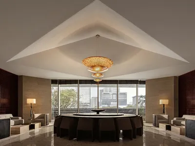 A modern hotel lobby features marble and concrete materials with a central dining table and seating areas.