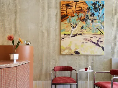 A modern restaurant lobby features a concrete reception desk with pink tiles and red cushioned chairs, alongside an abstract