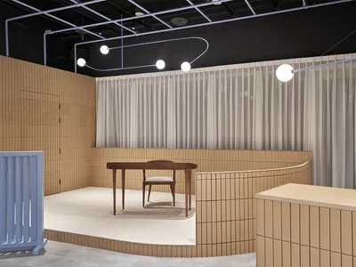A minimalist restaurant interior with beige tiles and white curtains, featuring a single wooden table and chair on a raised p