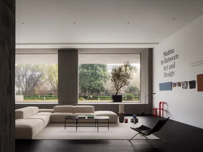 Minimalist living room with concrete walls and furniture, large windows overlooking greenery, and a modern coffee table.