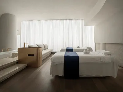 A minimalist bedroom with white, subtly textured walls and a dark wooden floor.