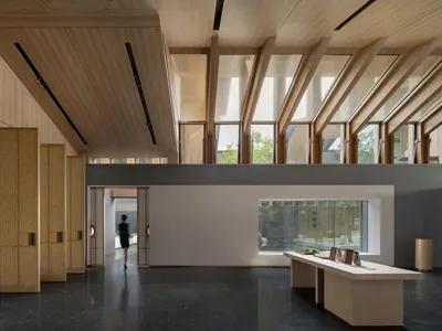 A modern hotel lobby with wooden walls and ceiling, a black marble floor, and large windows.