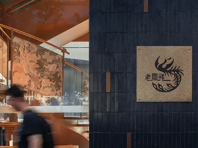 Modern restaurant exterior featuring black tiles and concrete materials, with a branded sign and staircase interior in the ba