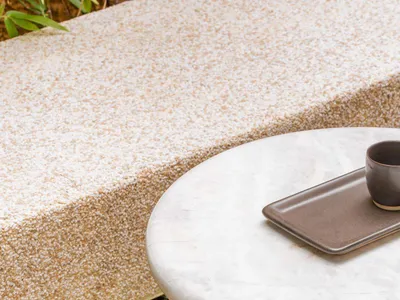 A round marble table with a tray and cup on a natural stone patio surrounded by greenery.