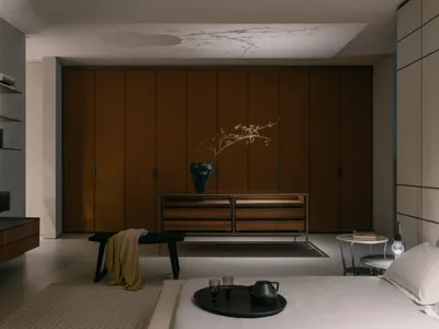 A minimalist bedroom featuring wooden furniture, a textured rug, and a decorative vase with dried branches, creating a serene