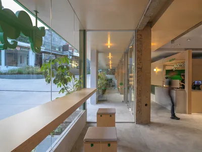 A modern coffee shop with concrete interior, featuring a large window displaying plants outside.
