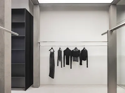 極簡服裝零售展示，黑色衣架上懸掛各式黑色服飾，置於金屬桿上。
