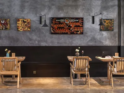 A cozy cafe interior with wooden chairs and concrete walls adorned with colorful art.