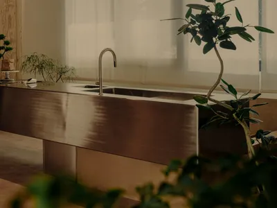 A contemporary kitchen interior features a sleek metal counter with a polished copper finish and a modern faucet.
