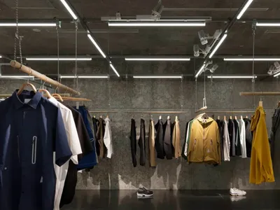服飾店內金屬衣桿懸掛多款外套與襯衫，搭配混凝土背景牆。