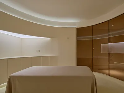 A minimalist bedroom with a glass wall and a large bed covered with a beige blanket.