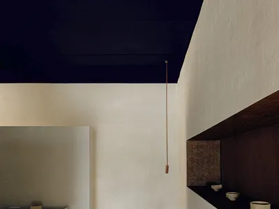A minimalist living room with concrete walls and floor, featuring a modern shelf with bowls and a blue-and-white vase.