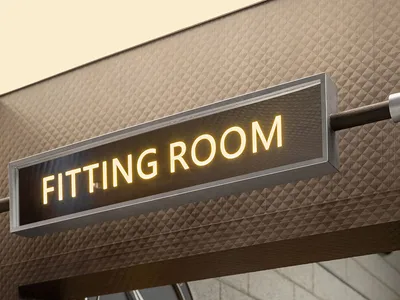 A sign indicating a fitting room entrance in a fashion retail interior with metallic materials.