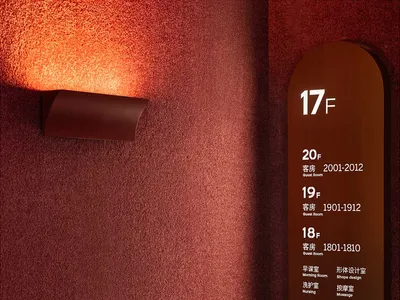 A textured wall with a light fixture and a sign indicating floor numbers and room numbers for hotel suites.