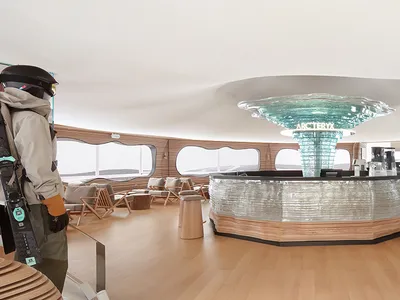 A spacious hotel interior featuring a central bar area with a glass dome ceiling, wooden flooring, and multiple seating optio