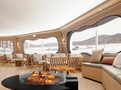 A modern lounge interior featuring a warm and inviting atmosphere with a wood-paneled room, cozy seating, and a central fire