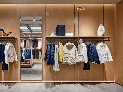 Retail shop featuring clothing displayed on wooden shelves and racks with a warm, minimalist design.