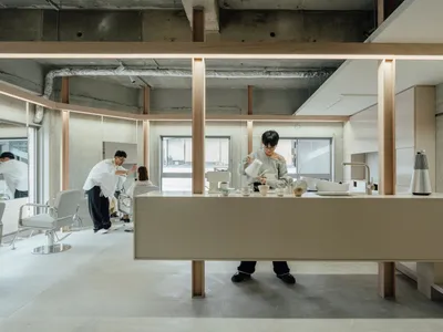 在極簡咖啡店中，有人正將咖啡倒入杯中，搭配混凝土材質的廚房吧台