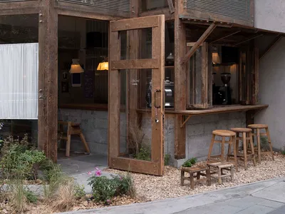 Wood and concrete exterior of a restaurant with large windows and open seating area.
