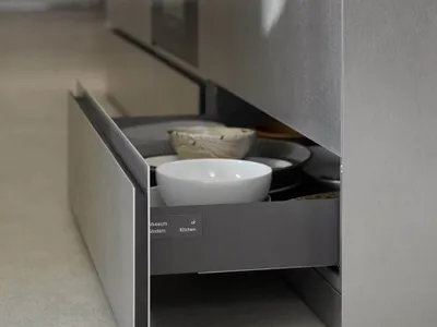 A modern kitchen with metallic cabinets and an open drawer filled with dishware.