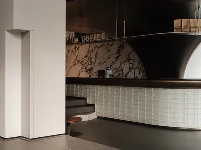 Modern minimalist coffee shop bar counter with white marble countertops and sleek, curved design.