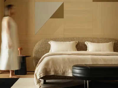 A modern minimalist bedroom featuring a bed with wooden headboard, leather ottoman, and wool bedding.