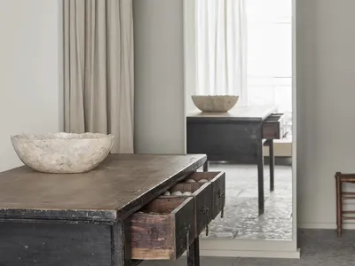 A modern home office setup featuring a wooden desk with an open drawer filled with small items, a large floor mirror, and a b