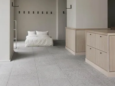 A minimalist bedroom features a white bed with a concrete floor