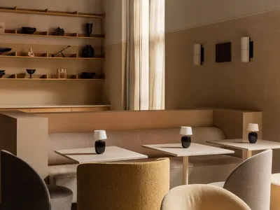 A minimalist restaurant interior featuring marble tables, fabric chairs, and wooden accents.