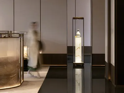 A spacious hotel lobby with sleek, metallic and glass design elements, illuminated by warm lighting.