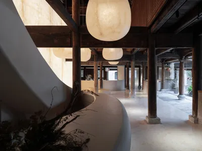 Wide-angle photograph of a sleek, contemporary hotel reception hall featuring concrete flooring, white walls, wooden beams, a
