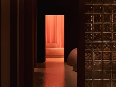 A dark, minimalist hotel room featuring metallic surfaces and a lounge area.