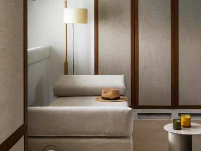 A minimalist bedroom with fabric elements, featuring a bed, floor lamp, and storage basket.