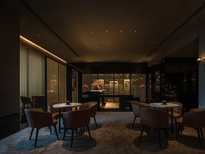 A modern restaurant lobby featuring dark-toned leather furniture and marble tables.