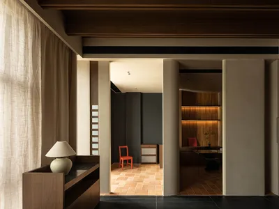 Modern home office with concrete walls and floor tiles, featuring wooden furniture and a red chair.