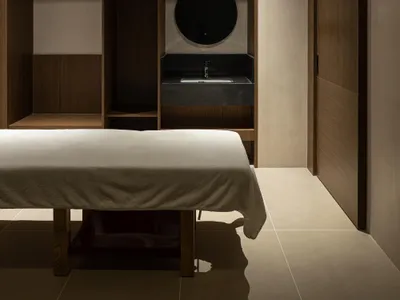 一間極簡臥室，配有白色床單的床、木質櫃體，以及附圓形鏡子和黑色檯面的水槽