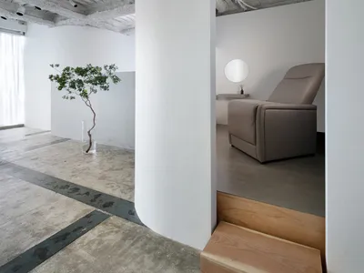 A minimalist living room with concrete floors and walls, featuring a gray recliner and a small potted plant.