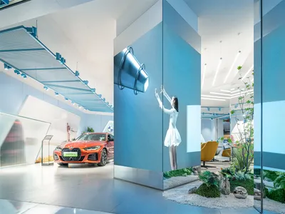 一座汽車展示間，採用現代室內設計，搭配藍色燈光、金屬裝飾與綠色植栽。