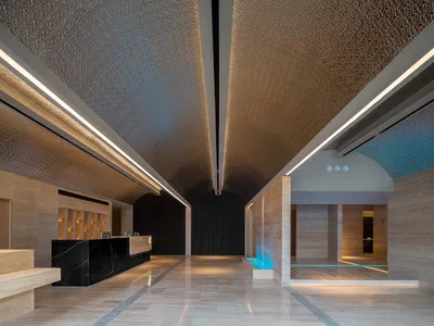 A modern hotel lobby featuring marble floors and walls, with a reception desk and a water feature.