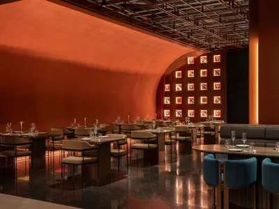 A photograph of a restaurant interior with metallic red walls and concrete tiles, showcasing modern lighting and furniture.